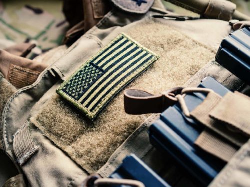 Green US flag patch on the tactical bulletproof vest with M4 magazines, selective focus